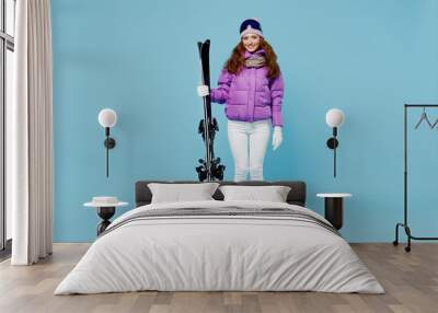 Full length skier fun cool caucasian woman 20s in warm purple padded windbreaker jacket goggles mask spend extreme weekend in mountains hug hold ski isolated on plain blue background studio portrait Wall mural