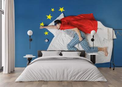 Full length top view powerful young man in pajamas jam sleep mask superhero suit rest relax home lies make fly gesture isolated on dark blue sky background Night bedtime supernatural abilities concept Wall mural