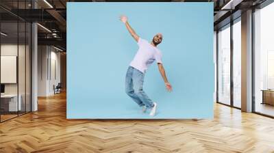 Full length young cool smiling happy funny unshaven black african man 20s wearing violet t-shirt hat glasses standing on toes leaning back dancing isolated on pastel blue background studio portrait. Wall mural