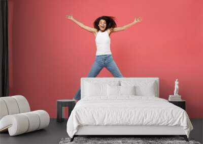 Full length young fun overjoyed happy joyful cheerful positive african american woman in casual white tank shirt jump high with outstretched hands isolated on pink color background studio portrait Wall mural