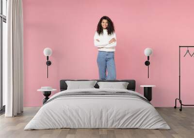 Full length young smiling african american woman 20s curly hair wear white casual knitted sweater jeans looking camera hold hands crossed folded isolated on pastel pink background studio portrait. Wall mural