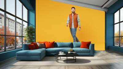 Full length young smiling happy confident smiling cheerful fun caucasian man 20s years old wear orange vest mint sweatshirt walking going looking camera isolated on yellow background studio portrait Wall mural