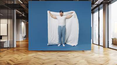 Full size body length happy young fun man in pajamas jam sleep mask rest relaxing at home wrap cover with blanket duvet look camera isolated on dark blue background Good mood night bedtime concept Wall mural