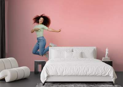 Full size body length young curly latin woman 20s wears casual clothes sunglasses jump point back on workspace area copy space mock up isolated on plain pastel light pink background studio portrait. Wall mural