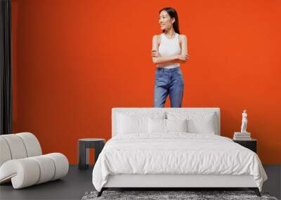 Full size excited jubilant exultant cheerful happy young woman of Asian ethnicity 20s years old in white tank top hold hands crossed looking aside isolated on plain orange background studio portrait. Wall mural