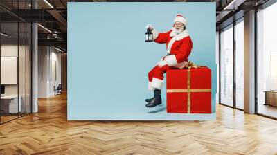 Full size old Santa Claus man in Christmas hat red suit clothes sitting on big gift present box hold lantern isolated on plain blue background studio Happy New Year 2022 merry ho x-mas holiday concept Wall mural