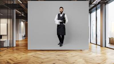 Full size young barista male waiter butler man 20s wear white shirt vest elegant uniform work at cafe hold bottle of wine isolated on plain grey background studio portrait Restaurant employee concept Wall mural