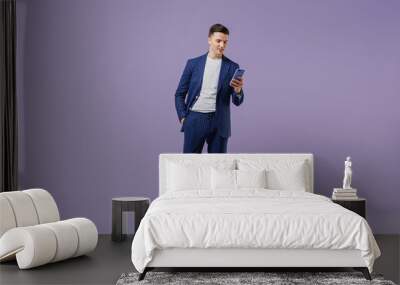 Full size young successful employee business man lawyer 20s wear formal blue suit white t-shirt move stroll hold use mobile cell phone hand in pocket isolated pastel purple background studio portrait. Wall mural