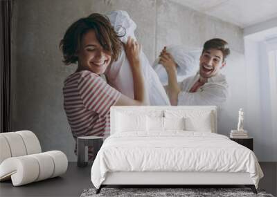 Fun young playful joyful couple two friend woman man 20s in casual clothes play on couch sofa fight pillows game fool around kidding laugh rest indoors at home flat together People lifestyle concept. Wall mural