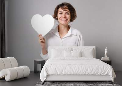 Funny attractive young business woman in white shirt posing isolated on grey wall background studio portrait. Like blogging social network concept. Mock up copy space. Hold white blank empty heart. Wall mural