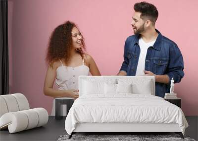 Funny couple two friends european guy african american girl in casual clothes isolated on pastel pink background. People lifestyle concept. Mock up copy space. Looking at each other, speaking talking. Wall mural