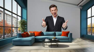 Funny screaming young business man in classic black suit shirt posing isolated on grey background studio portrait. Achievement career wealth business concept. Mock up copy space. Showing thumbs up. Wall mural