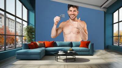 Funny young bearded fitness sporty strong guy bare-chested muscular sportsman posing isolated on blue background. Workout sport motivation lifestyle concept. Hold credit bank card, showing thumb up. Wall mural