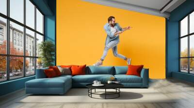 Funny young bearded man in casual blue shirt posing isolated on yellow orange background, studio portrait. People emotions lifestyle concept. Mock up copy space. Jumping pointing index fingers aside. Wall mural