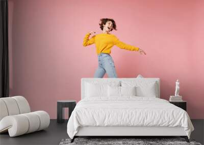 Funny young brunette woman girl in yellow sweater posing isolated on pastel pink background in studio. People lifestyle concept. Mock up copy space. Having fun fooling around, looking aside, jumping. Wall mural