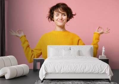 Funny young brunette woman girl in yellow sweater posing isolated on pastel pink background. People lifestyle concept. Mock up copy space. Hold hands in yoga gesture relaxing meditating looking aside. Wall mural