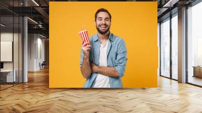 Funny young man in casual blue shirt posing isolated on yellow orange wall background, studio portrait. People sincere emotions lifestyle concept. Mock up copy space. Hold in hand cup of soda or cola. Wall mural