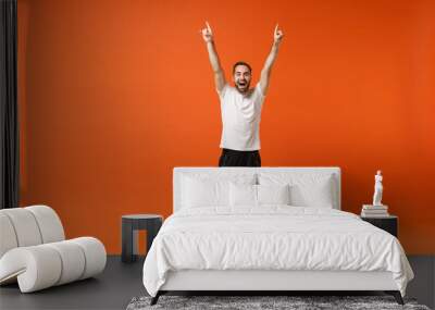 Funny young man in casual white t-shirt posing isolated on orange background, studio portrait. People sincere emotions lifestyle concept. Mock up copy space. Rising hands, pointing index fingers up. Wall mural