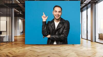 Handsome stylish young unshaven man in black jacket white t-shirt showing on workspace isolated on blue wall background studio portrait. People sincere emotions lifestyle concept. Mock up copy space. Wall mural