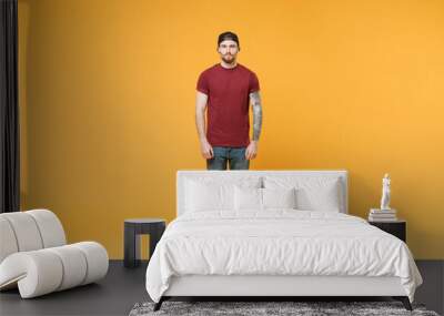 Handsome young tattooed man guy in casual t-shirt black cap posing isolated on yellow wall background studio portrait. People sincere emotions lifestyle concept. Mock up copy space. Looking camera. Wall mural