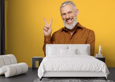 Happy excited elderly gray-haired bearded man 40s years old wear brown shirt looking camera showing victory sign isolated on plain yellow background studio portrait. People emotions lifestyle concept Wall mural