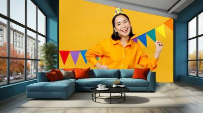 Happy fun cheerful smiling young woman wearing casual clothes hat celebrating near bunting flags gesticulating hands dancing isolated on plain yellow background. Birthday 8 14 holiday party concept. Wall mural