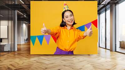 Happy fun satisfied young woman wears casual clothes hat celebrating near bunting flags show thumb up stretch hands to camera isolated on plain yellow background. Birthday 8 14 holiday party concept. Wall mural