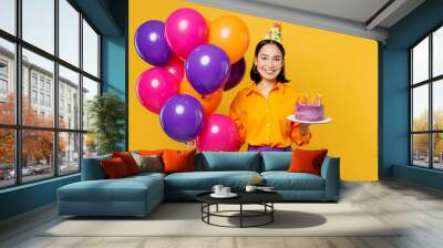 Happy fun young woman wears casual clothes hat celebrating hold bunch of colorful air balloons cake with candles look camera isolated on plain yellow background. Birthday 8 14 holiday party concept. Wall mural