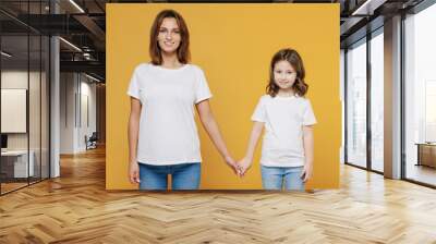 Happy woman in basic white t-shirt have fun with child baby girl 5-6 years old hold hands. Mom little kid daughter isolated on yellow orange color background studio. Mother's Day love family concept. Wall mural