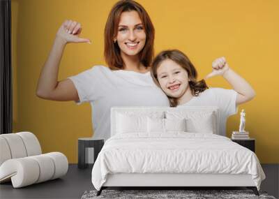 Happy woman in white t-shirt with child baby girl 5-6 years old point thumbs on themselves. Mom little kid daughter isolated on yellow orange color background studio. Mother's Day love family concept. Wall mural