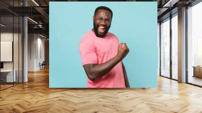 Happy young african american man guy in casual pink t-shirt posing isolated on pastel blue background studio portrait. People emotions lifestyle concept. Mock up copy space. Doing winner gesture. Wall mural