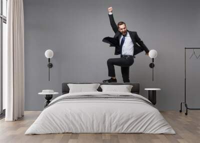 Happy young business man in classic black suit shirt tie posing isolated on grey background. Achievement career wealth business concept. Mock up copy space. Jumping, doing winner gesture, screaming. Wall mural