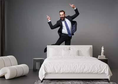 Happy young business man in classic black suit shirt tie posing isolated on grey background. Achievement career wealth business concept. Mock up copy space. Jumping, point index fingers up, screaming. Wall mural