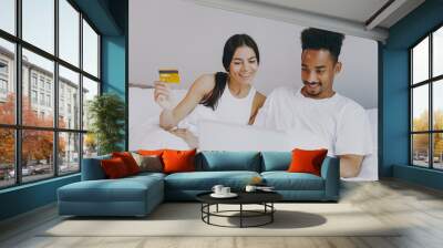 Happy young couple two friends family man woman in casual white clothes sit in bed using laptop pc computer hold credit bank card spend time together in bedroom lounge home house wake up good day Wall mural