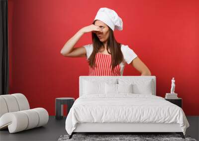 Housewife female chef cook or baker in striped apron, white t-shirt, toque chefs hat isolated on red wall background. Housekeeper woman close nose with hand because smell. Mock up copy space concept. Wall mural