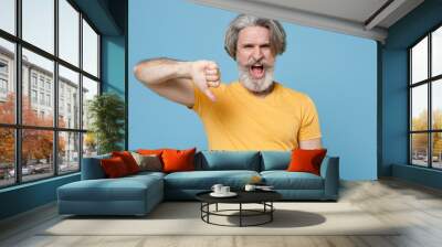 irritated elderly gray-haired mustache bearded man in casual yellow t-shirt posing isolated on blue  Wall mural