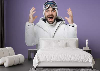 Irritated skier man in white windbreaker jacket ski goggles mask spreading hands screaming swearing spend weekend winter in mountains isolated on purple background. People lifestyle hobby concept. Wall mural