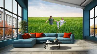 Joyful man, woman walk on green field background, rest, have fun, play, run with little cute child baby boy. Mother, father, little kid son. Family day 15 of may, love, parents, children concept. Wall mural