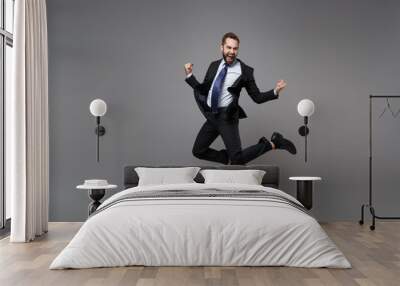 Joyful young business man in classic black suit shirt tie posing isolated on grey background. Achievement career wealth business concept. Mock up copy space. Jumping, doing winner gesture, screaming. Wall mural