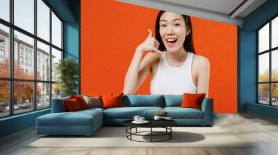 Jubilant blithesome charismatic stunning young woman of Asian ethnicity 20s years old in white tank top doing phone gesture like says call me back isolated on plain orange background studio portrait. Wall mural