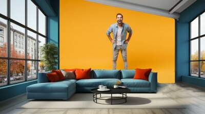 Laughing young bearded man in casual blue shirt posing isolated on yellow orange background, studio portrait. People emotions lifestyle concept. Mock up copy space. Standing with arms akimbo on waist. Wall mural