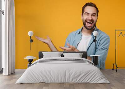 Laughing young bearded man in casual blue shirt posing isolated on yellow orange wall background, studio portrait. People sincere emotions lifestyle concept. Mock up copy space. Pointing hands aside. Wall mural