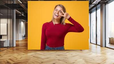 Laughing young blonde woman girl in casual clothes posing isolated on yellow orange background studio portrait. People emotions lifestyle concept. Mock up copy space. Showing victory sign, blinking. Wall mural