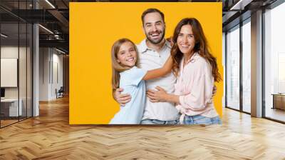 Laughing young happy parents mom dad with child kid daughter teen girl in basic t-shirts hugging looking camera isolated on yellow background studio portrait. Family day parenthood childhood concept. Wall mural