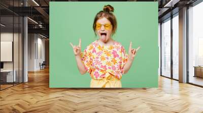 Little child kid girl 6-7 years old wear casual clothes sunglasses do horns up gesture, depicting heavy metal rock sign isolated on plain green background. Mother's Day love family lifestyle concept. Wall mural