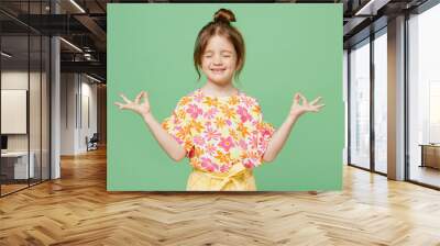 Little child kid girl 6-7 years old wearing casual clothes hold spread hands in yoga om aum gesture relax meditate try calm down isolated on plain green background . Mother's Day love family concept. Wall mural