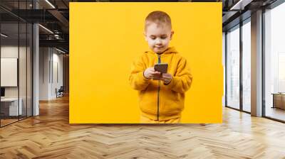 Little cool kid boy 3-4 years old in yellow clothes talking on mobile phone isolated on orange wall background, studio portrait. Problem of children and gadgets. Lifestyle concept. Mock up copy space. Wall mural