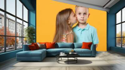 Little couple kids boy girl 5-6 years old in blue pink clothes shirt dress posing have fun isolated on yellow background children studio portrait. People childhood lifestyle concept kiss cheek love Wall mural