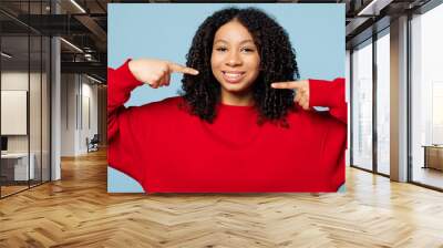 Little happy kid teen girl of African American ethnicity wear red sweatshirt point fingers on toothy smile white teeth isolated on pastel plain light blue cyan background. Childhood lifestyle concept. Wall mural