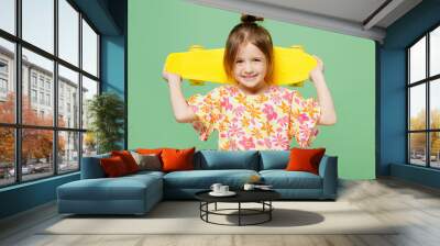 Little smiling happy child kid girl 6-7 years old wear casual clothes have fun hod in hand skateboard look aside on area isolated on plain green background. Mother's Day love family lifestyle concept Wall mural